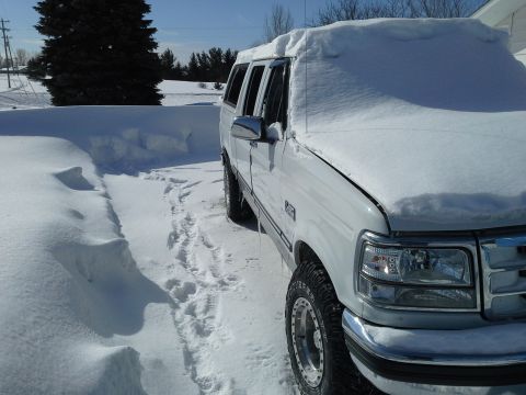 1996 Ford Bronco - A white Ford truck, likely a 1992 model, is partially covered in snow with a camper shell on the bed.