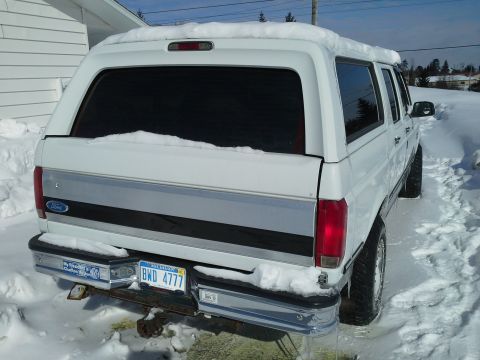 1996 Ford Bronco - A white 1996 Ford Bronco with a camper shell sits covered in snow, displaying its rear and license plate.