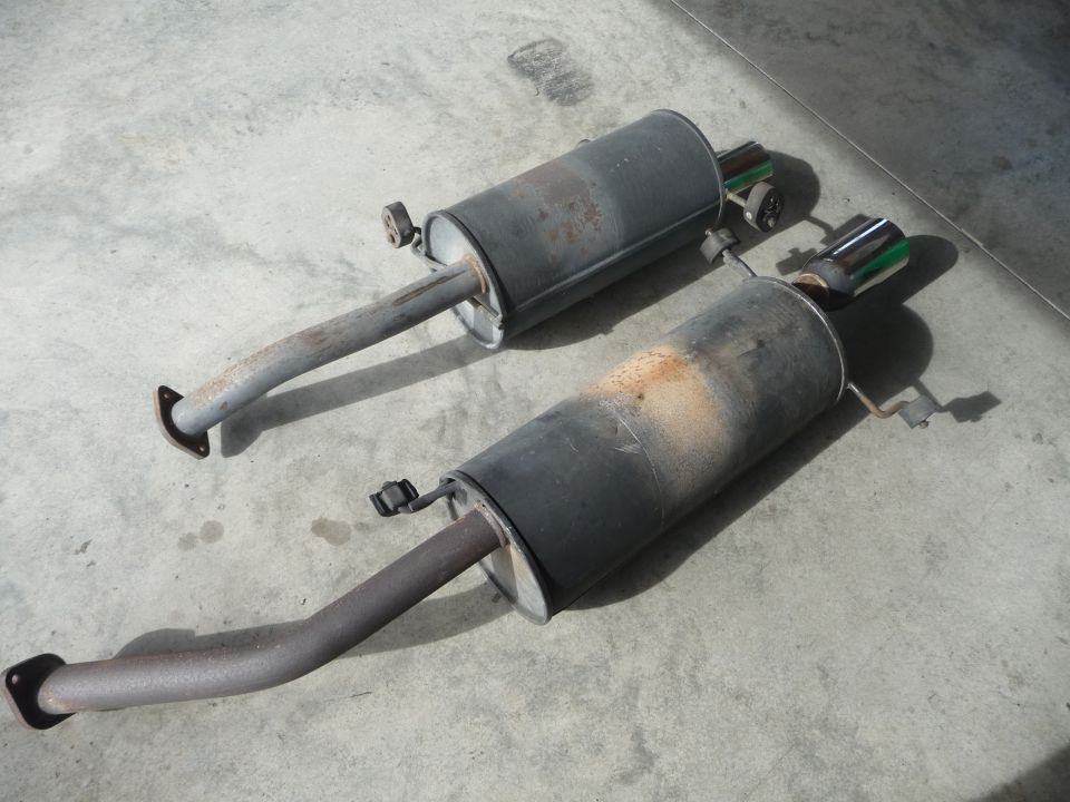 Two used exhaust mufflers with chrome tips, resting on a concrete surface