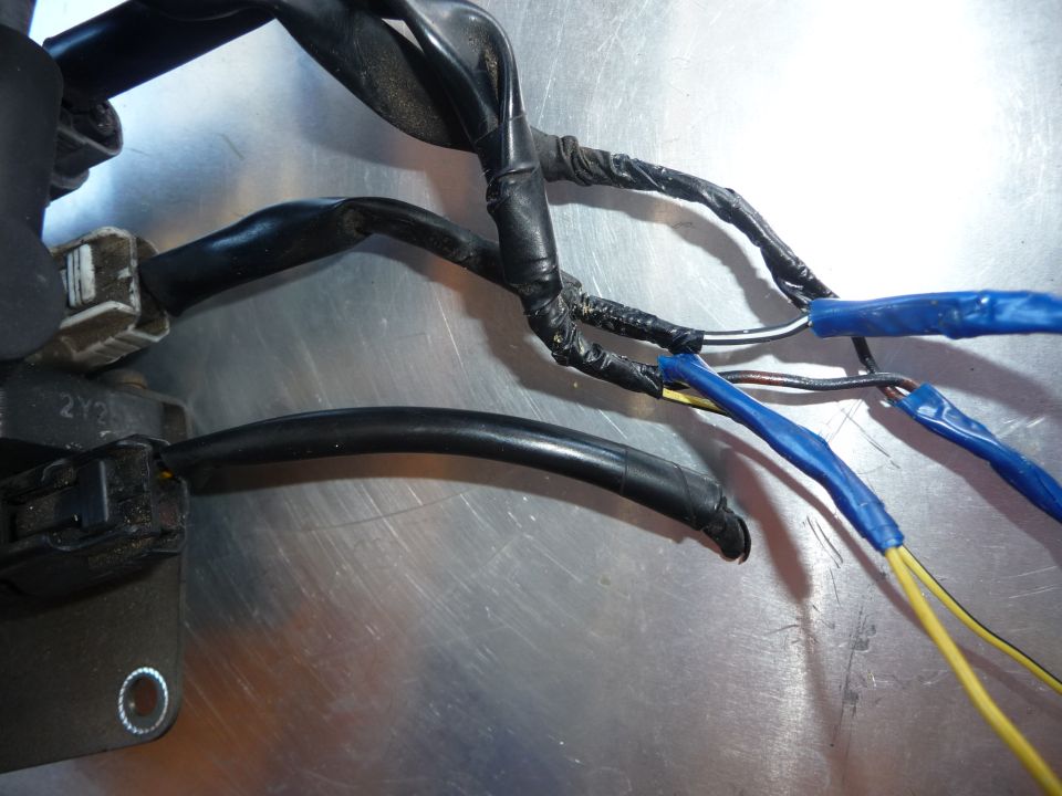 Close-up of a vehicle wiring harness with black tape and blue electrical tape on exposed wires