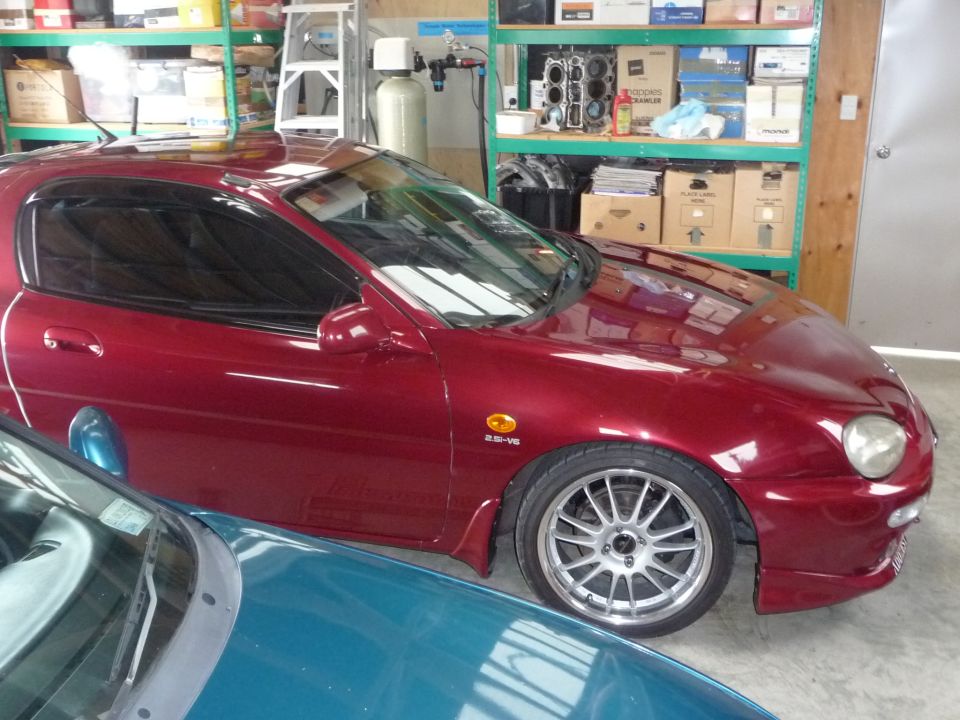 1993 Mazda MX-3, 2.5-V6 badge visible, parked next to a teal car in a garage