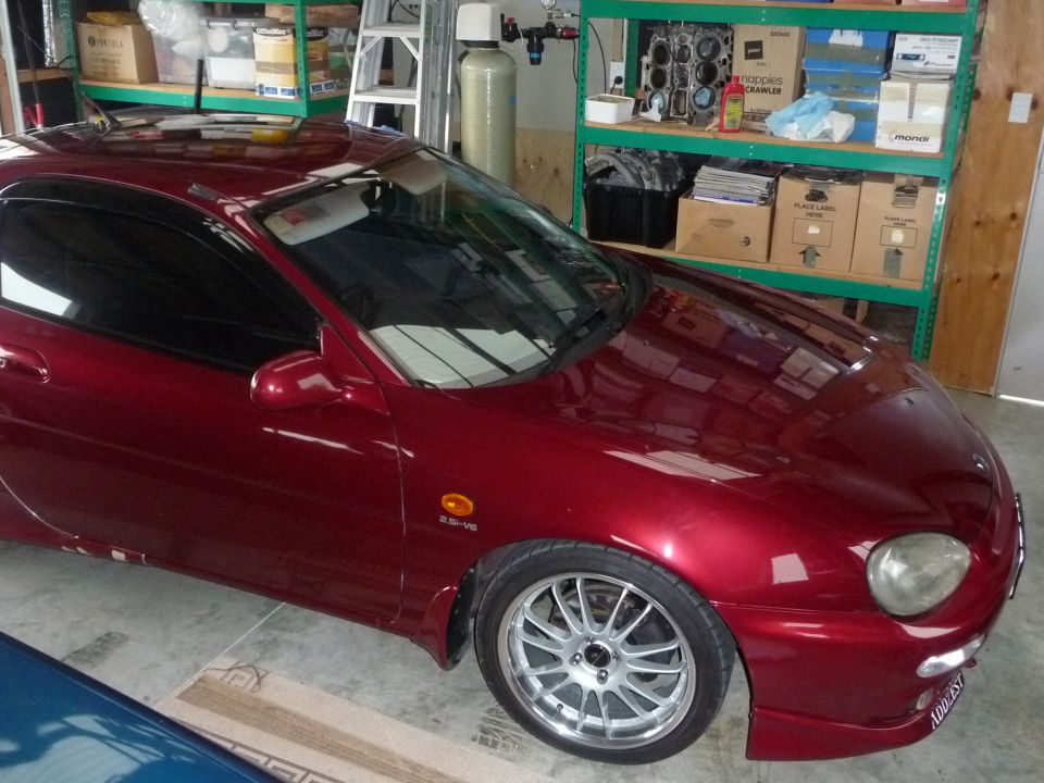 Red 1993 Mazda MX-3 coupe, 3/4 front view, parked indoors