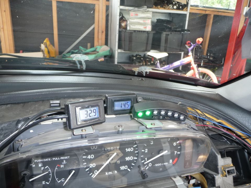 Car dashboard interior with digital gauges showing 32.9 and 14.5, and a multi-gauge with green lights