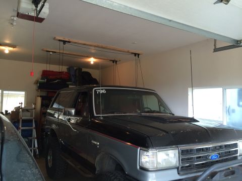 1989 Ford Bronco - A two-tone Ford Bronco is parked in a garage with storage shelves and a garage door opener visible.