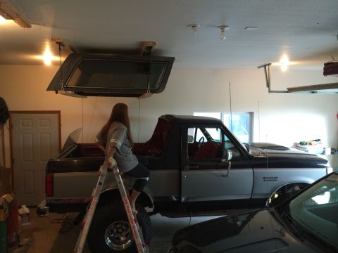 1989 Ford Bronco - A two-tone Ford Bronco is parked in a garage, with a camper shell suspended above it.
