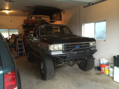 1989 Ford Bronco - This lifted Ford F-Series truck is parked in a garage with its removable top stored overhead.