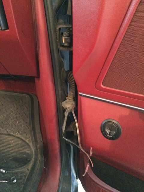 1989 Ford Bronco - Exposed wiring and a speaker are visible in the door jamb of a vehicle with red interior panels.