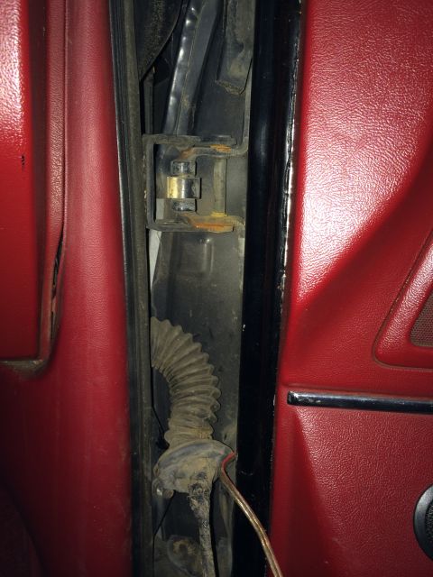 1989 Ford Bronco - Close-up of a vehicle's door hinge and wiring, showing red interior paneling and signs of rust.