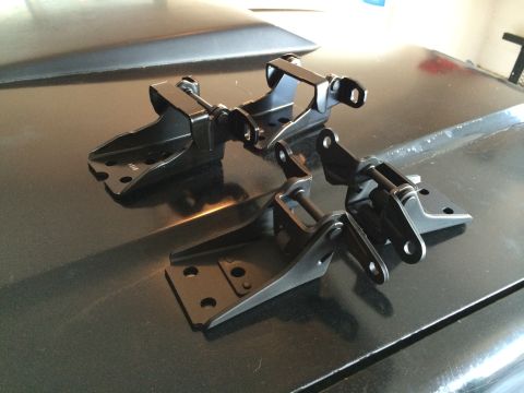1989 Ford Bronco - Four black hood hinges are displayed on a dark, reflective surface, possibly a car hood.