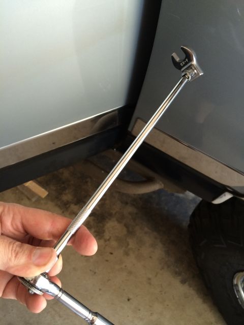 1989 Ford Bronco - Close-up of a hand holding a small ratchet wrench with a socket, positioned near a vehicle's door and tire.