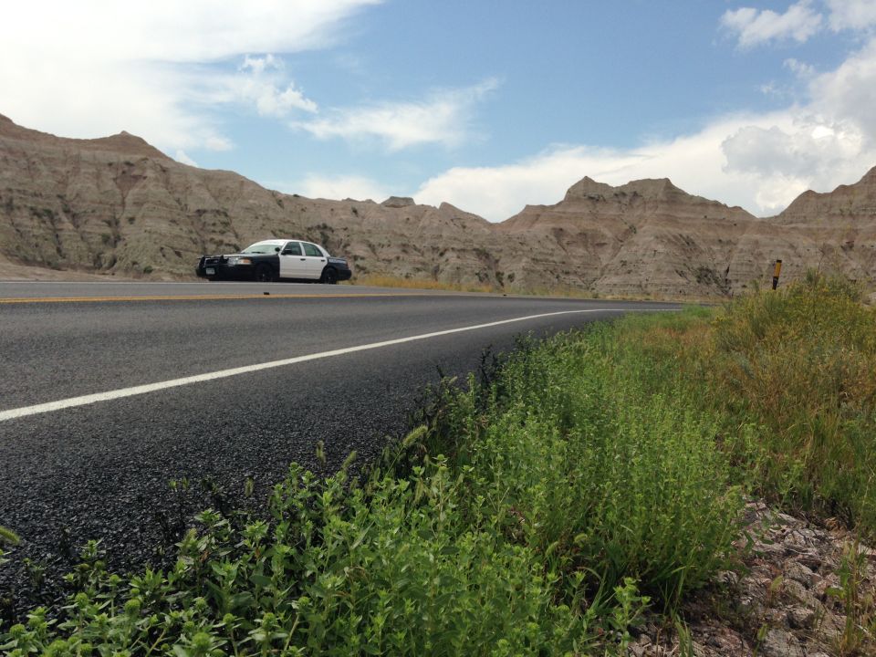 Police car parked on the side of a road in a rocky, desert landscape