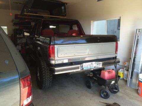 1989 Ford Bronco - Rear view of a lifted Ford Bronco with a trailer hitch and a red gas can on a cart.