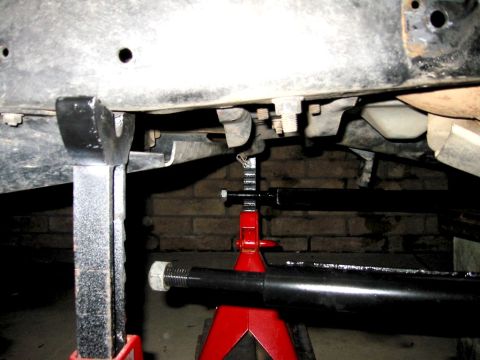 1985 Ford Bronco - Underneath view of a vehicle being supported by jack stands, with a brick wall in the background.
