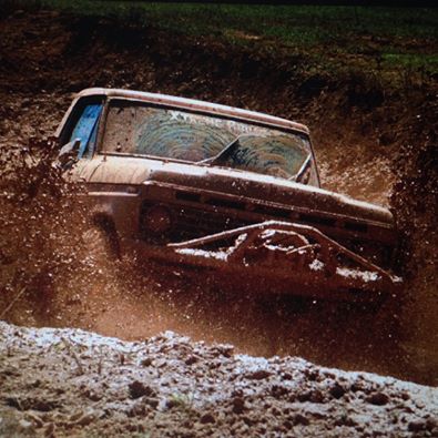 1978 Ford Bronco - A 1978 Ford Bronco navigates a muddy terrain, kicking up a significant amount of dirt and water.