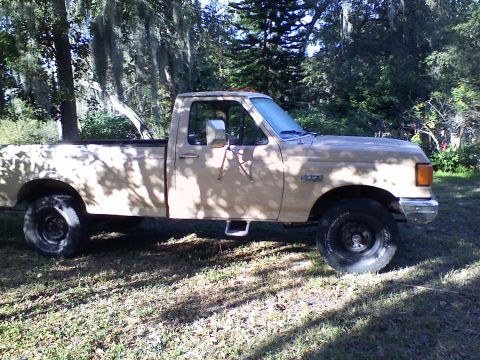 1990 Ford F-250 - A tan 1987 Ford F-250 pickup truck is parked outdoors on a grassy area with trees in the background.