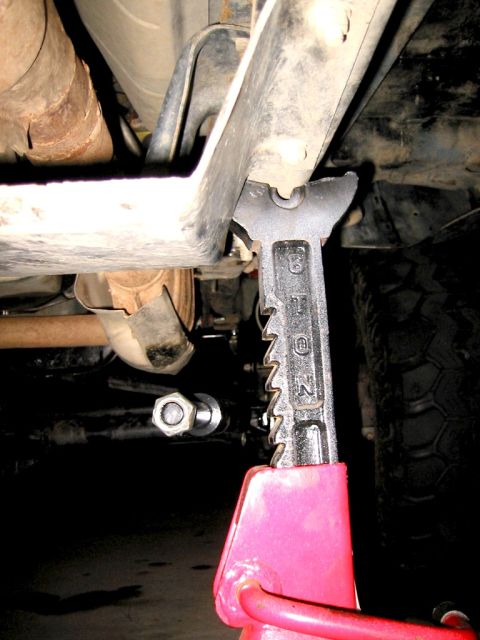 1985 Ford Bronco - A vehicle's undercarriage is shown supported by a red jack, with visible exhaust and suspension parts.