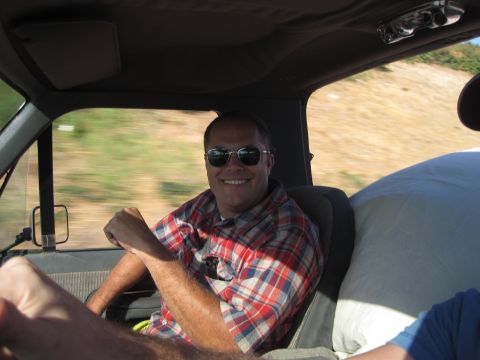 1989 Ford Bronco - A man smiles while driving a vehicle, with a passenger and cargo visible.