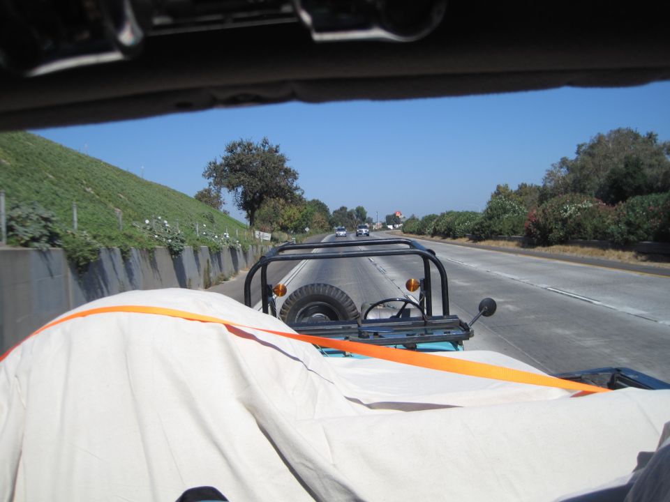 View from inside a Jeep CJ-7 driving on a highway, showing the spare tire and roll cage. Another vehicle is visible ahead