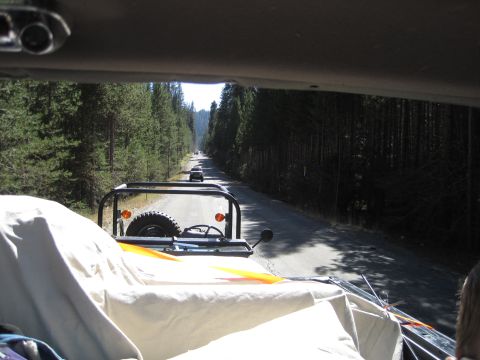 1989 Ford Bronco - A convoy of vehicles travels down a tree-lined dirt road, viewed from the interior of the lead vehicle.