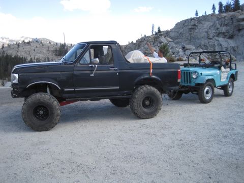 1989 Ford Bronco - A person in the Bronco waves while it tows a Jeep through a rocky, mountainous area.