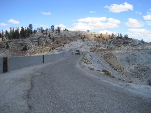 1989 Ford Bronco - A lone SUV navigates a winding road through a , mountainous landscape under a partly cloudy sky.