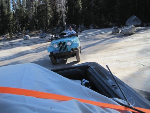 1989 Ford Bronco - A blue Jeep CJ is driven on a rocky, unpaved road in a wooded area.