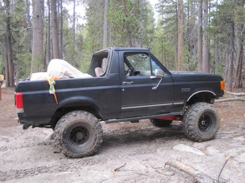 1989 Ford Bronco - A black Ford Bronco with off-road modifications sits in a wooded area.