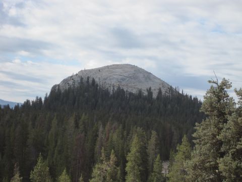 1989 Ford Bronco - A scenic view of a mountain peak surrounded by a dense forest under a cloudy sky.