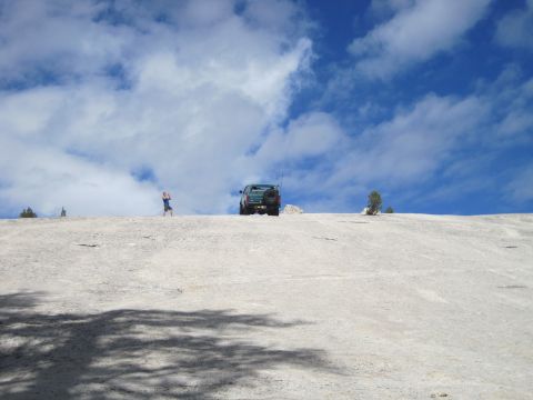 1989 Ford Bronco - SUV parked on a rocky surface with a person nearby and a cloudy blue sky above.