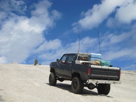 1989 Ford Bronco - A modified pickup truck with multiple antennas is parked on a rocky, barren landscape under a blue sky with scattered clouds.