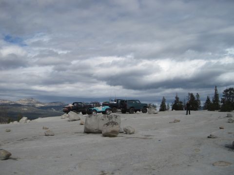 1989 Ford Bronco - A group of off-road vehicles are parked on a rocky expanse under a dramatic, cloudy sky.