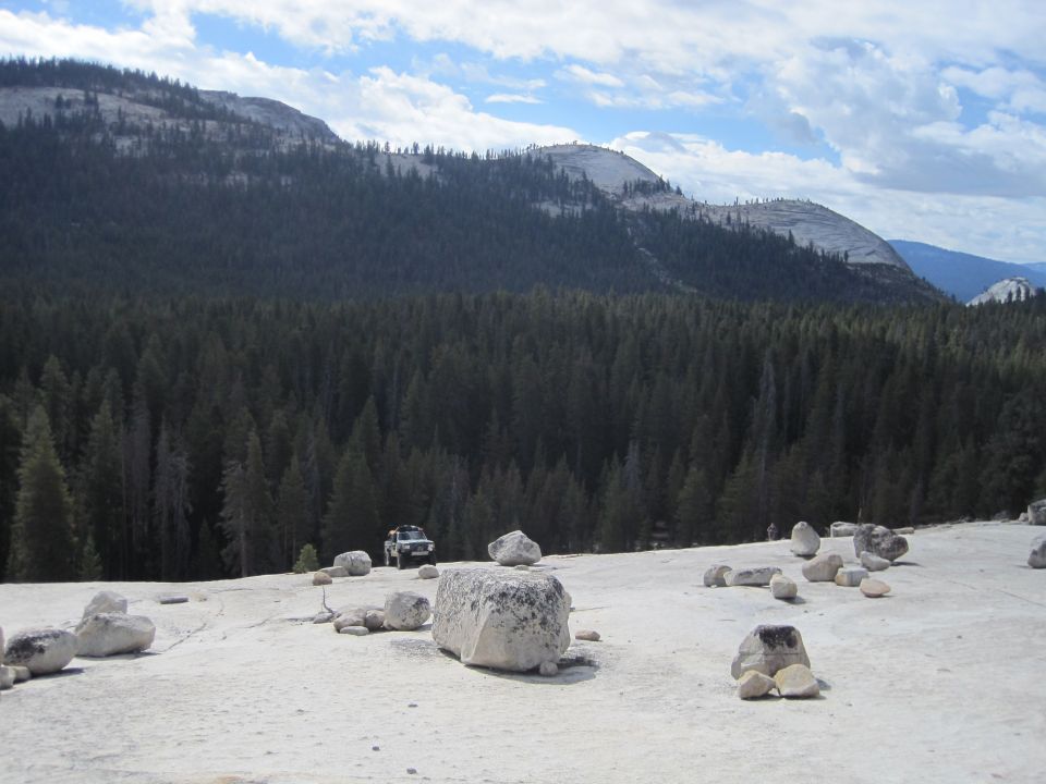 Off-road vehicle parked on a large, flat rock surface with a dense forest and mountains in the background