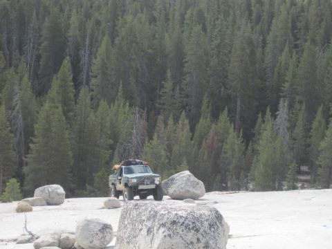 1989 Ford Bronco - A modified pickup truck is parked in a rocky area with a dense forest behind it.