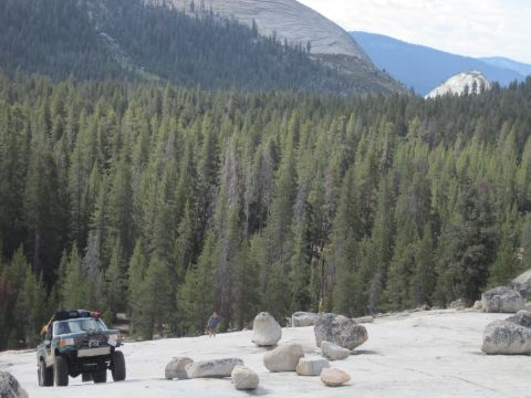 1989 Ford Bronco - A green 1987 Ford Bronco navigates a rocky terrain surrounded by dense pine forest and mountains.