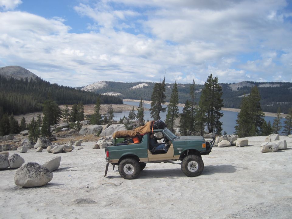1989 Ford Bronco parked on rocky ground, lake and trees behind