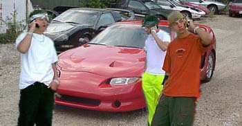 1994 Ford Crown Victoria - Three men are on cell phones in front of a red sports car, with other vehicles in the background.