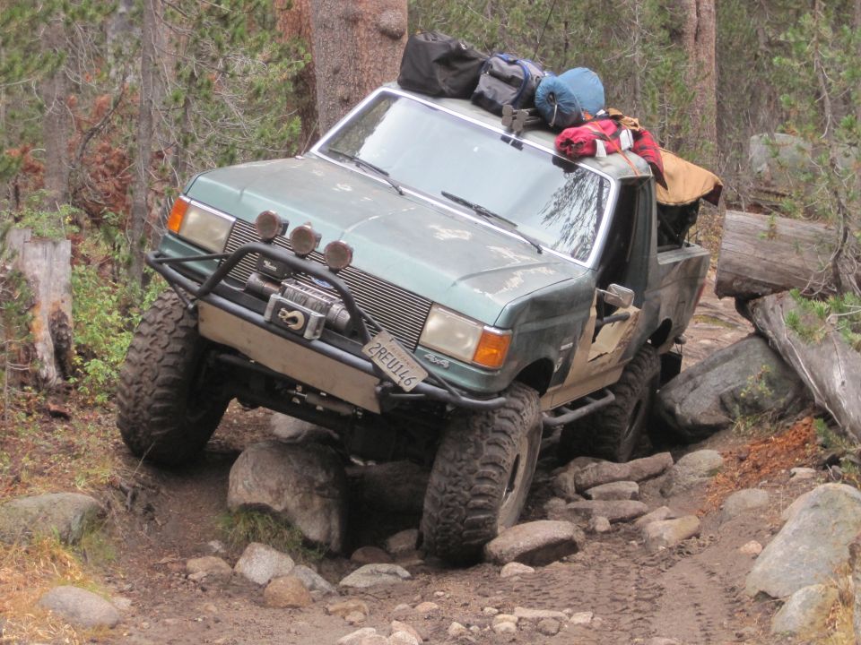 1989 Ford Bronco on rocky trail, loaded with camping gear on roof