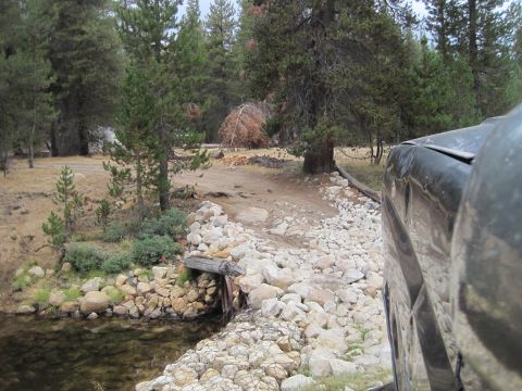 1989 Ford Bronco - A vehicle navigates a rough, rocky path near a stream in a wooded area.