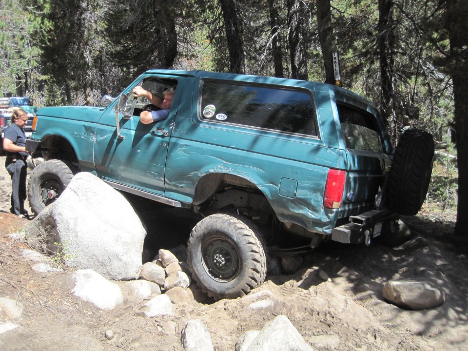 Teal SUV with off-road tires navigating rocks and dirt, driver visible