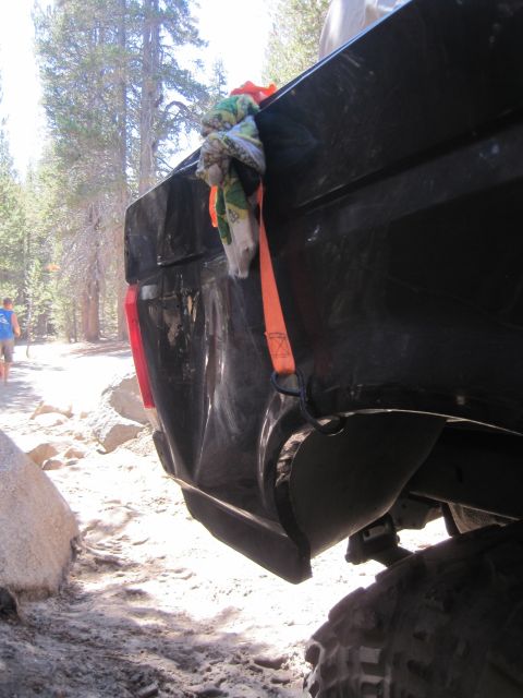 1989 Ford Bronco - The rear corner of a black pickup truck shows significant damage, secured with an orange strap.
