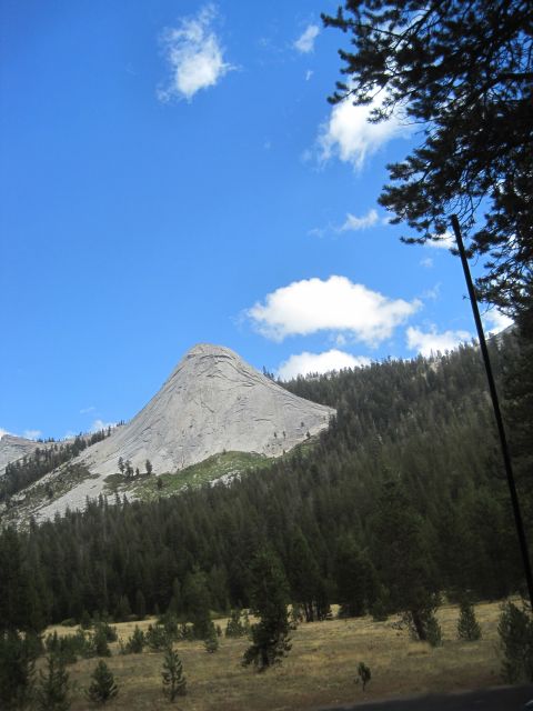 1989 Ford Bronco - A vast mountain landscape unfolds with a prominent granite dome, surrounded by a thick forest and a sun-drenched meadow.