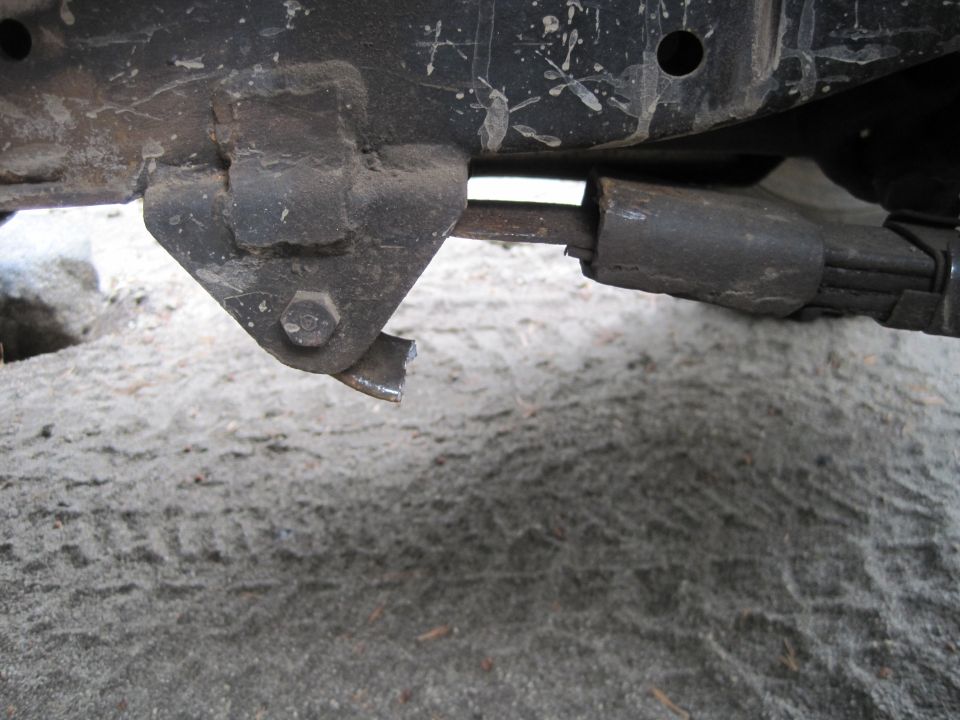 Close-up of a damaged metal bracket on a vehicle's suspension system, with a leaf spring visible