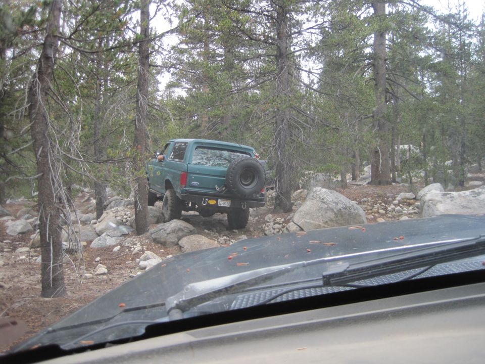 Green SUV with spare tire on rear door, off-roading on a rocky trail