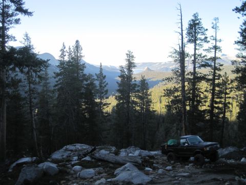 1989 Ford Bronco - A black Ford Bronco is parked on a rocky trail, surrounded by trees, with a mountainous landscape visible in the distance.