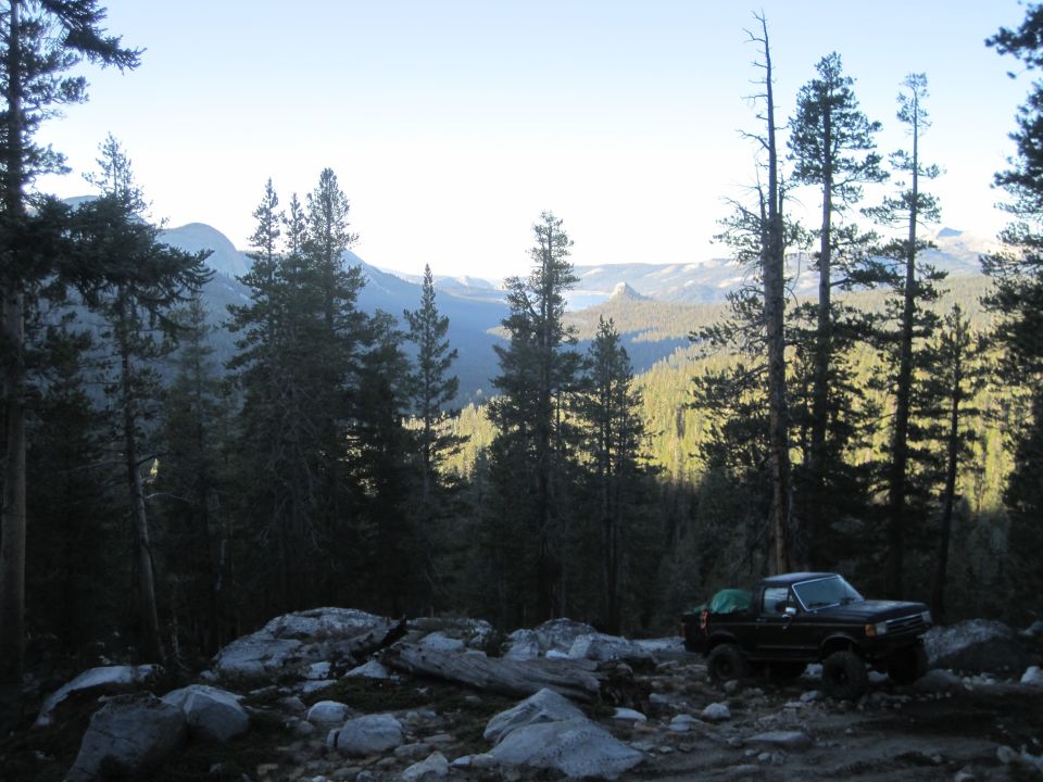 Black Ford Bronco parked on a rocky, wooded trail with mountains in the background
