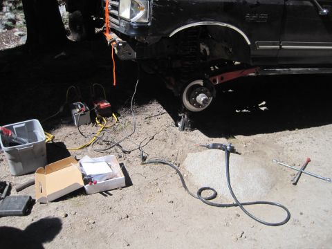 1989 Ford Bronco - A black Ford truck is undergoing maintenance, with its front wheel off and tools laid out on the ground.
