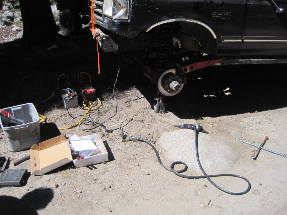 Black Ford truck with front wheel removed, jacked up, with batteries and tools nearby