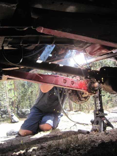 1989 Ford Bronco - A person welds suspension components on the underbody of a vehicle outdoors.