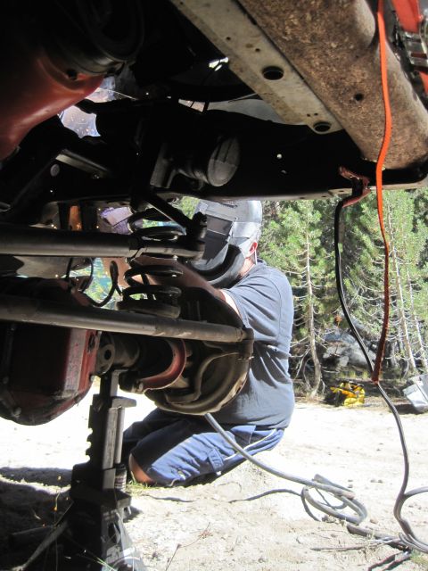 1989 Ford Bronco - A person is welding on the underside of a vehicle that is supported by jack stands.