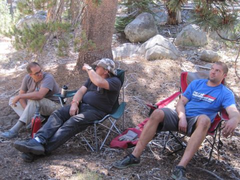 1989 Ford Bronco - Three men are seated in camping chairs in a wooded area, with one man pointing towards something off-camera.